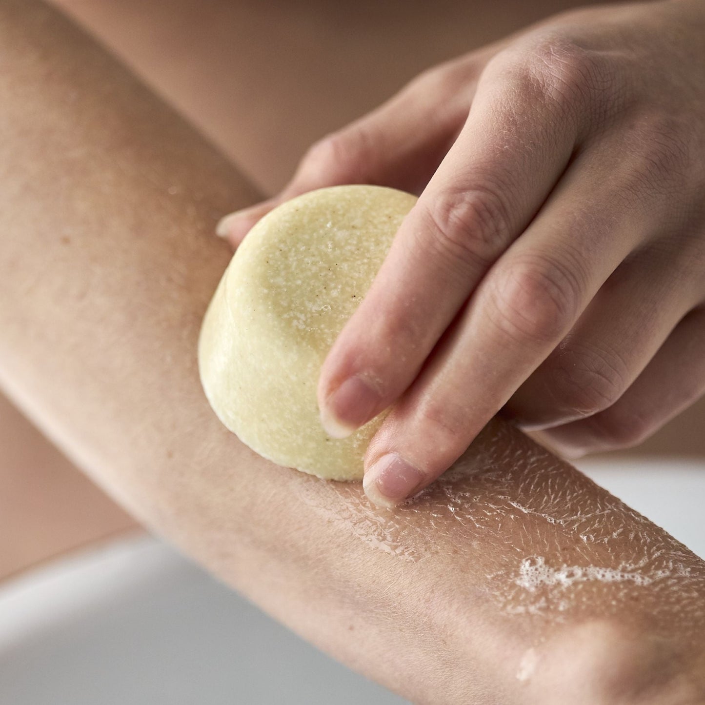 En hånd påfører en sæbebar direkte på armen.